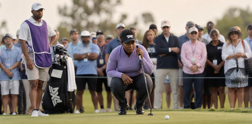 A gallery of fans watching a player line up a putt at a HERitage Golf Tour event